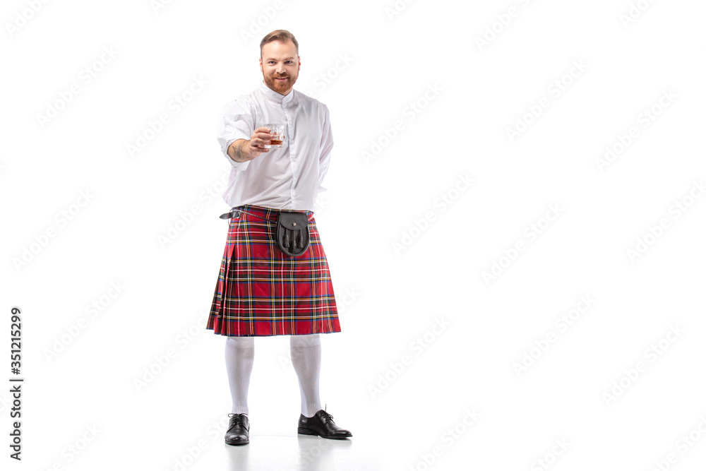 smiling Scottish redhead man in red kilt with whiskey in glass on white background smiling Scottish redhead man in red kilt with whiskey in glass on white background