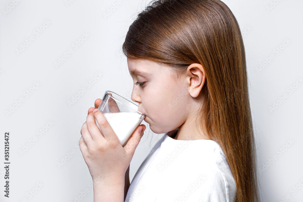 The girl drinks white milk from a transparent glass. Cute baby child with a cup of milk. Products for human health. Kid with a cup of milk. World international milk day. Copy space for text The girl drinks white milk from a transparent glass. Cute baby child with a cup of milk. Products for human health. Kid with a cup of milk. World international milk day. Copy space for text