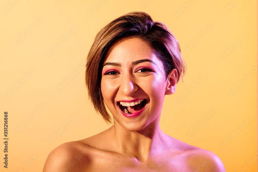 Soft skin smiling beautiful woman with short hair on a yellow background iluminated with purple light
