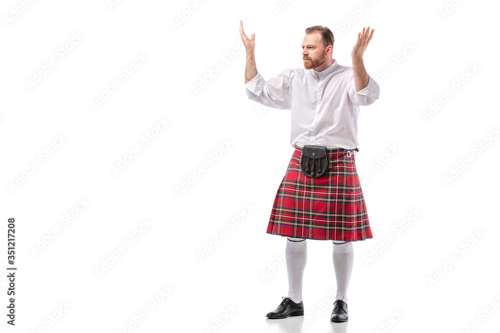 Scottish redhead bearded man in red tartan kilt showing shrug gesture on white background Scottish redhead bearded man in red tartan kilt showing shrug gesture on white background