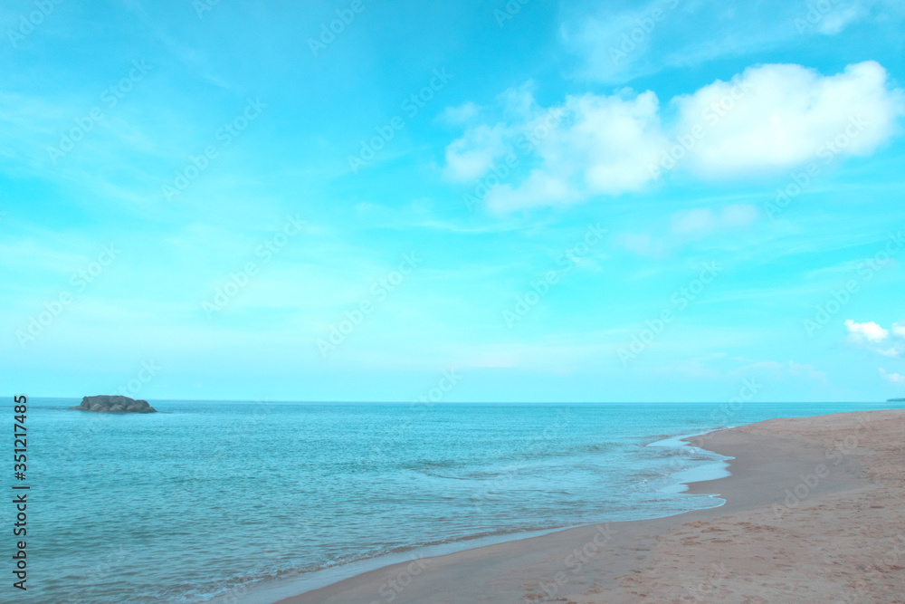 Beautiful calm ocean waves reaching tropical sandy beach on sunny blue sky background with puffy fluffy clouds & white cloudscape in morning sunlight & sun rays at daylight sunshine day, free space  
