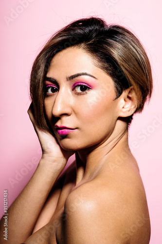 Looking at camera portrait of a beautiful woman with soft skin on a pink background