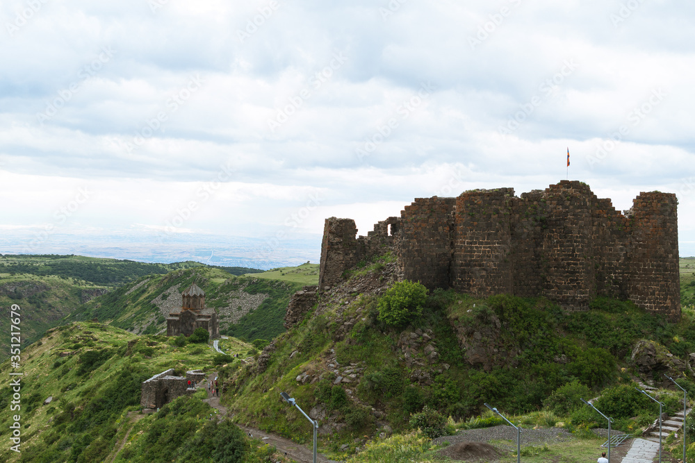 Old defensive fortress on hilltop. Mountain landscape with green meadows and stone castle in cloudy weather
