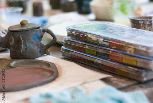 Watercolor in the plastic box set pile up on the table beside ceramic work elephant mug