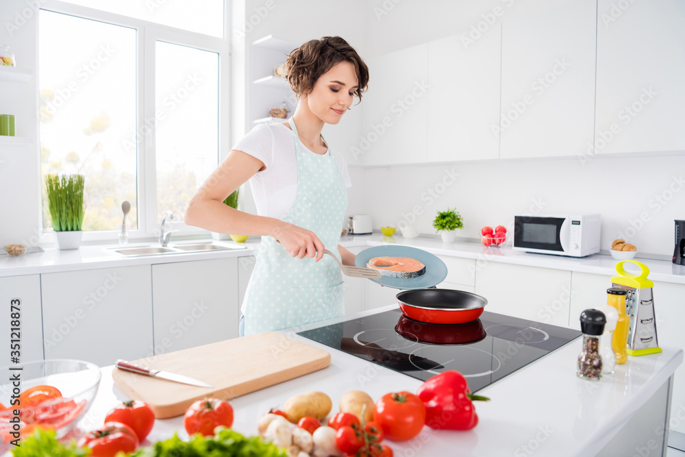Photo of beautiful housewife lady putting fresh raw salmon fillet steak on flying pan keeping diet morning cooking wear apron t-shirt stand modern kitchen indoors