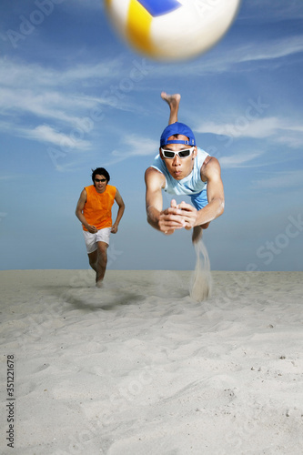 Man diving to hit volleyball, man running in the background