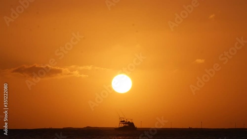 Stunning time lapse of a sunset with a moving cloud, the sun disappearing behind the horizon right in front of a big shaking fisher boat in Cabo Verde photo