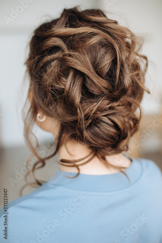 Complex hairstyle on the head of a brown-haired woman, rear view close-up. Fashionable professional women's hairstyle.