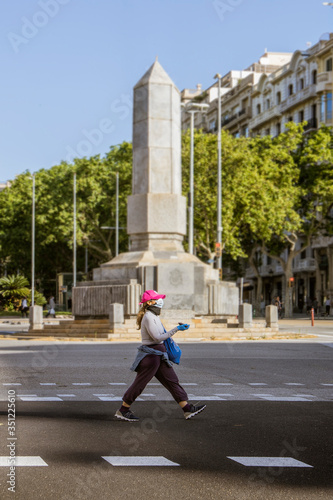 Woman walking alone in the empty streets under the sanitary measures, gloves and mask to avoid covid-19 / coronavirus. First walks around the city.