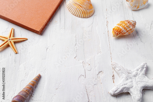Brown open notepad surrounded by sea shells on white wooden table closeup
