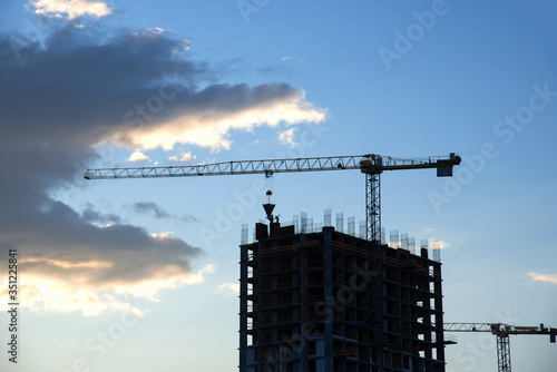 Tower crane in action on blue sky background. Preparing to pour a bucket of concrete into formwork. Сrane lifting cement bucket during construction a multi-storey residential building