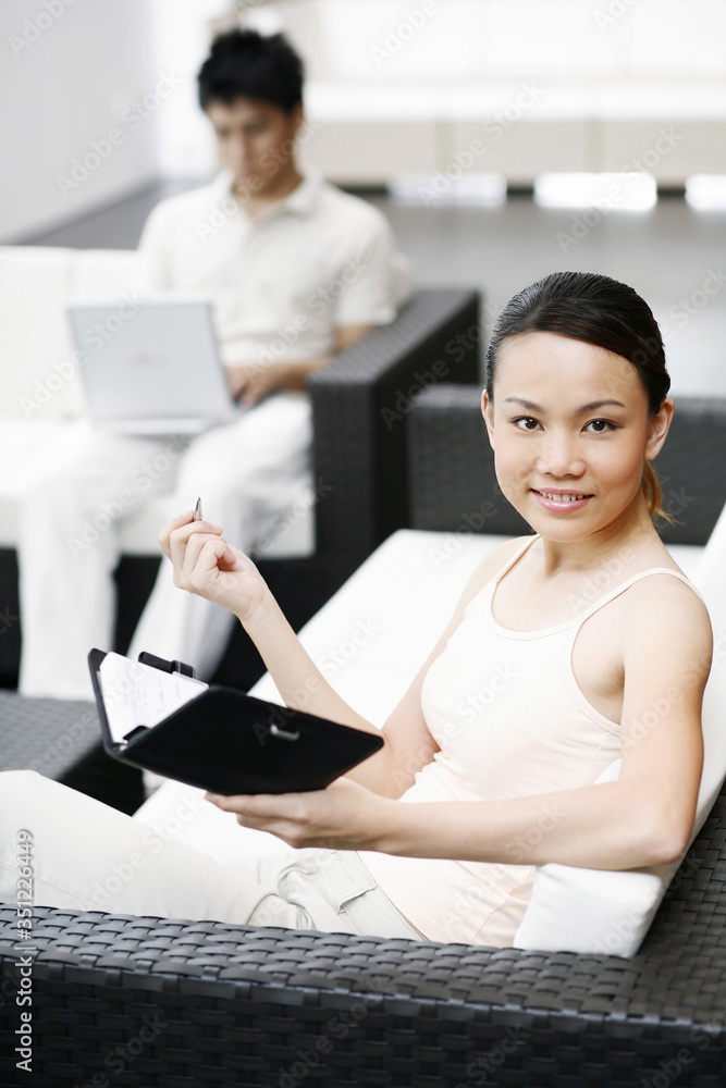 Obraz premium Woman writing diary with man using laptop in the background