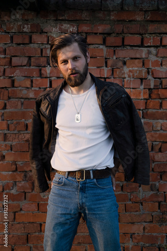 Bearded man posing against a brick wall.