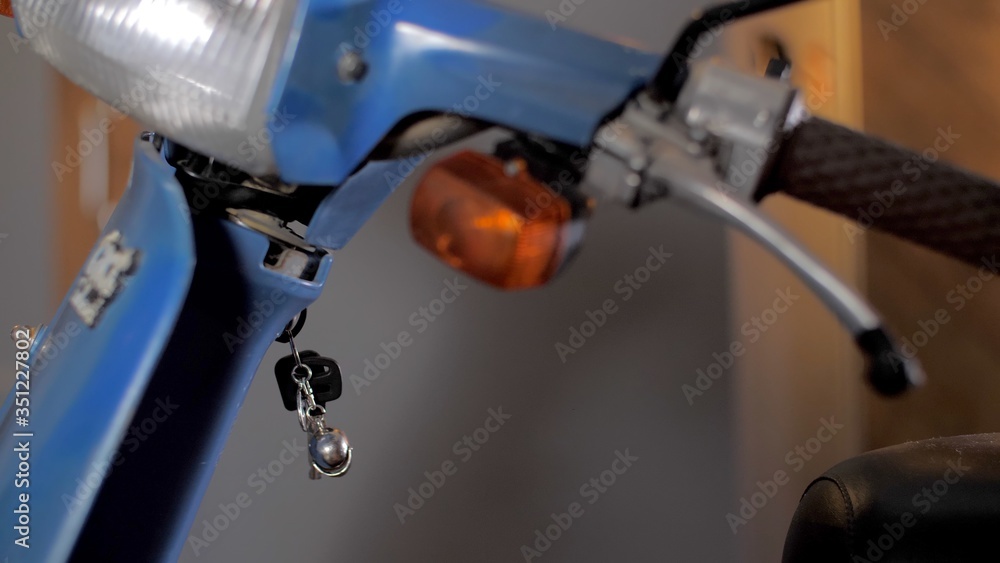 Close-up motorcycle wheel. Keys hanging in the ignition. Street sports bike stands in a modern home garage. Home brick garage. Blue moped or motorcycle. Self-isolation due to coronavirus. Close-up motorcycle wheel. Keys hanging in the ignition. Street sports bike stands in a modern home garage. Home brick garage. Blue moped or motorcycle. Self-isolation due to coronavirus.