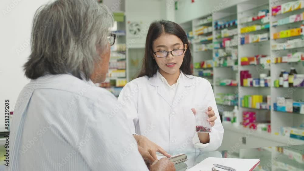 Beautiful asian Pharmacist explaining the medication to male senior patient in drug store Beautiful asian Pharmacist explaining the medication to male senior patient in drug store