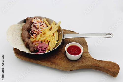 Lulia kebab in a pan with potatoes in pita bread with vegetables and sauce on a white background