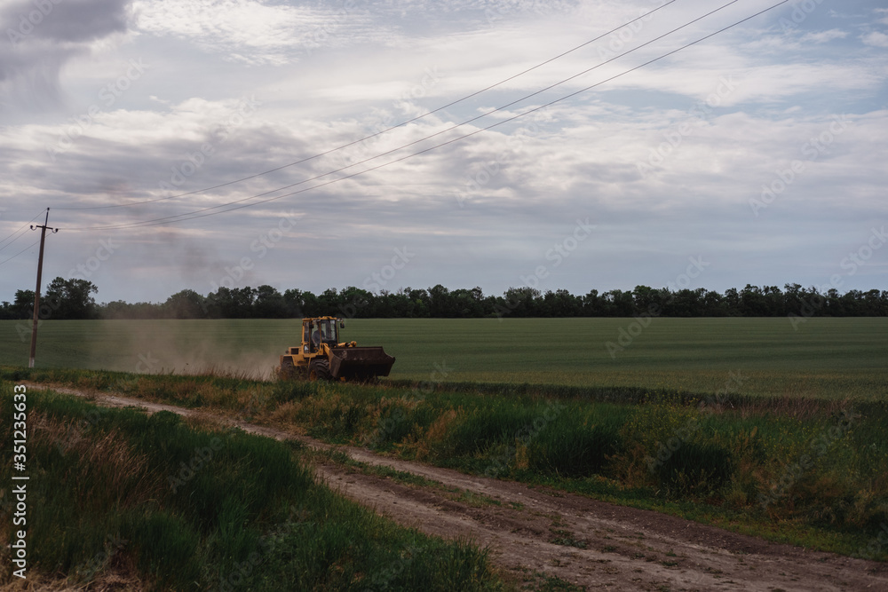 Fototapeta premium Yellow tractor rides on a green field.