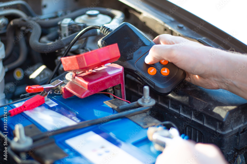 a car mechanic under the hood of a car diagnoses a car battery with a tester,repair and replacement of the battery