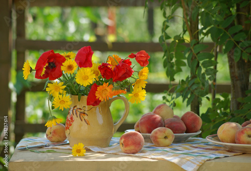 Still life with ripe peaches and a bright red-orange bunch of poppies and calendula flowers