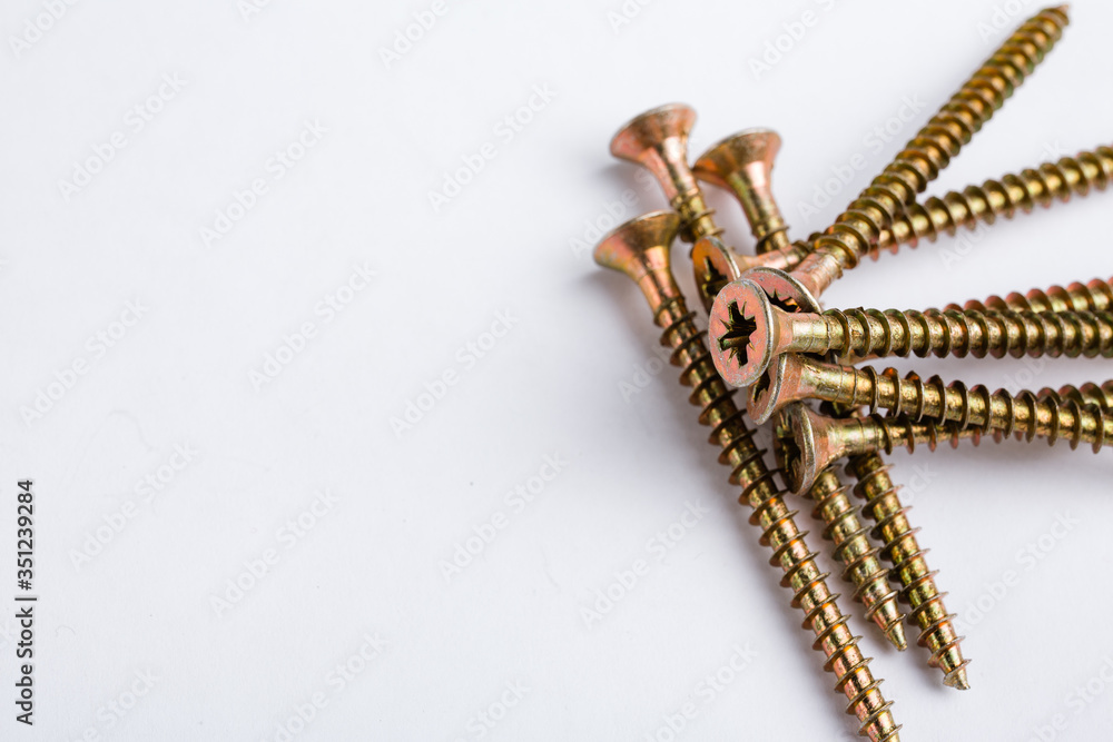 Gold wood screws lie on top of each other in the right corner on a white background. Space for text. Repair concept