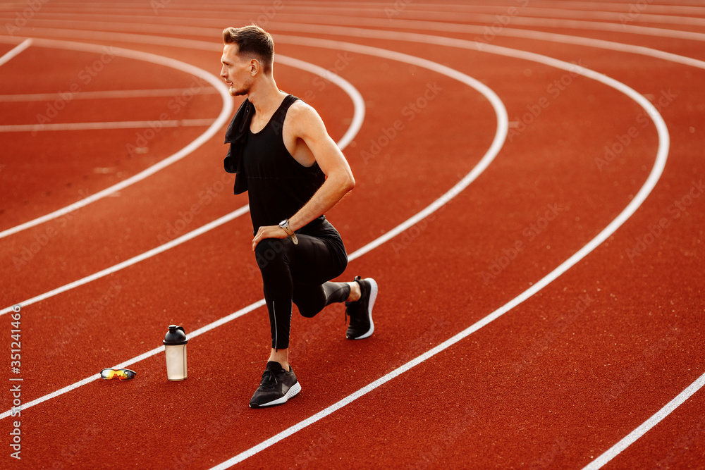 Obraz premium Young handsome man doing stretching before running in the stadium