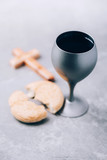 Unleavened bread, chalice of wine, wooden cross on grey background. Christian communion for reminder of Jesus sacrifice. Easter passover. Eucharist concept. Christianity symbol and faith