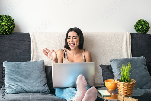 Young woman making video call sitting on sofa - Happy girl having fun doing video conference with family and friends - Youth millennial people lifestyle and technology concept photo
