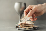 Hands with chalice and communion matzo bread, wooden cross on grey background. Christian communion for reminder of Jesus sacrifice. Easter passover. Eucharist concept. Christianity symbol and faith