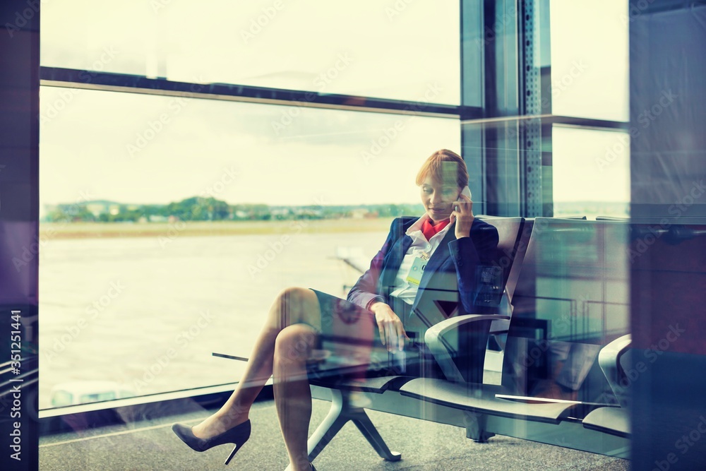 Photo of young attractive airport staff sitting while talking on smartphone

