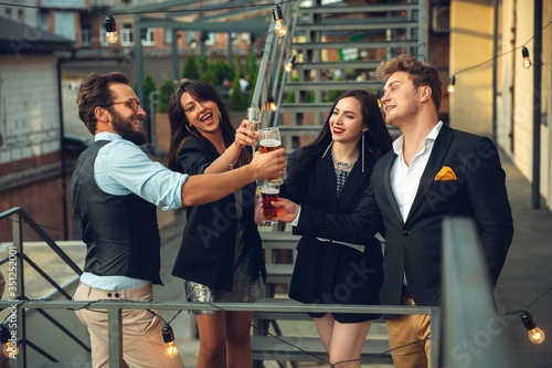 Success. Young people celebrating, look happy, have party at office or bar. Men and women drinking alcohol, talking, laughting. Holidays, weekend, business and finance, friendship concept
