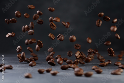 Many roasted coffee beans flying in the air. Selective focus. Coffee beans on a background of gray granite wall and table
