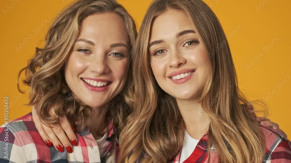 Young girls happy friends sisters isolated over yellow wall background hugging Young girls happy friends sisters isolated over yellow wall background hugging