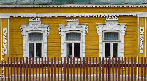 A row of small hunters with carved platbands in the yellow wall of a village house  