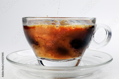 dark Coffee poring white milk dripping splash shadow liquid swirl in glass cup saucer on white background