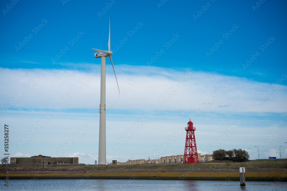 Red lighthouse and a Wind turbine on the Dutch Shore with a blue cloudy sky