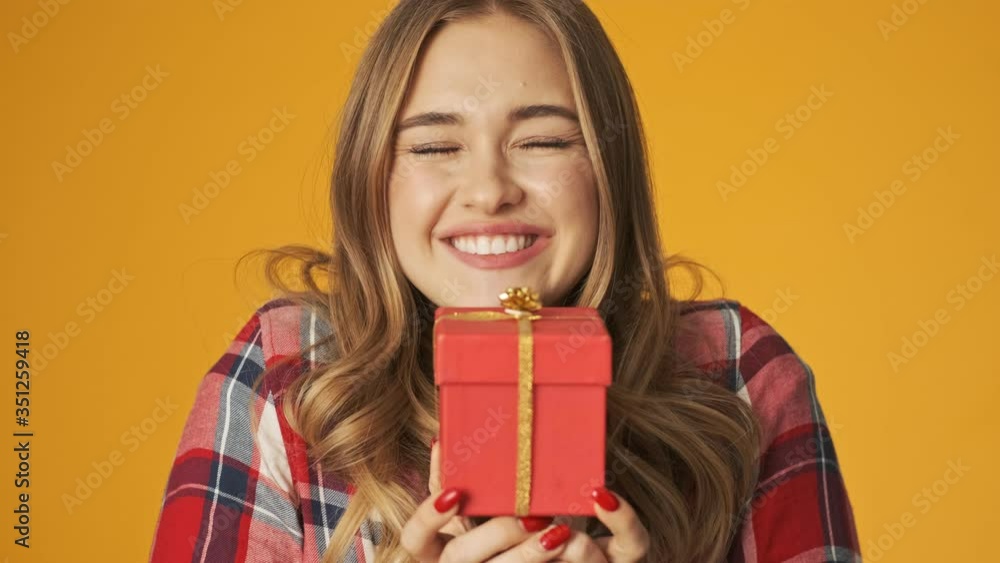 Young happy positive girl isolated over yellow wall background holding present box Young happy positive girl isolated over yellow wall background holding present box
