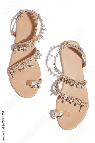 Detailed shot of beige flat sandals with toe ring and decorated with rhinestones and pearls. The pair of summer footwear is isolated on the white background. 