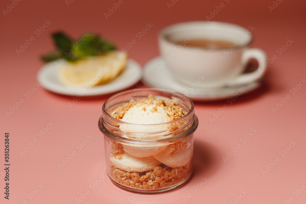 ice cream with crumble, next to a cup of tea and sliced lemon on a pink background ice cream with crumble, next to a cup of tea and sliced lemon on a pink background