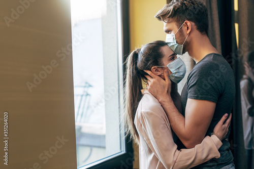 selective focus of man in medical mask kissing forehead of woman at home