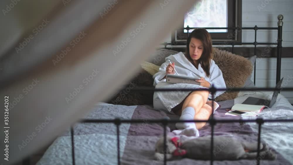 A young, beautiful girl lies in a bathrobe on the bed. Pretty woman working on a laptop. Sunny morning at home. A young, beautiful girl lies in a bathrobe on the bed. Pretty woman working on a laptop. Sunny morning at home.