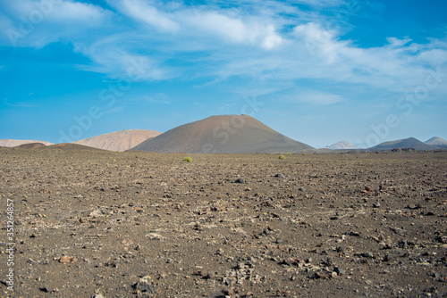 Empty rocky landscape on Lanzarote island on a sunny day with a blue cloudy sky 