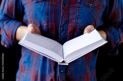 A mock-up of a white book in the hands of a man in a blue shirt