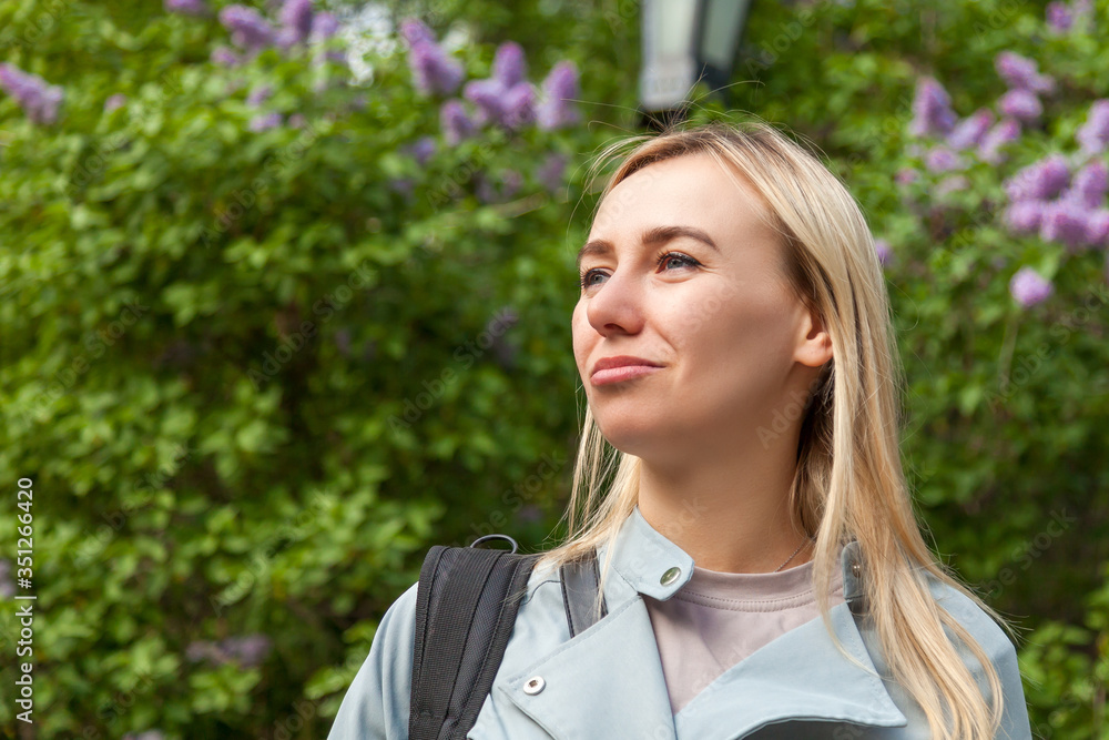Close-up face a blond girl background green bushes of lilac with pensive confident eyes looking up and side with blue eyes. Calm and confidence in the expectation of a new life during summer holidays. Close-up face a blond girl background green bushes of lilac with pensive confident eyes looking up and side with blue eyes. Calm and confidence in the expectation of a new life during summer holidays.