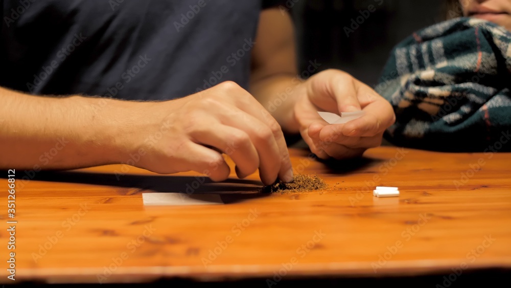 Hands making a cigar with tobacco. Man makes handmade cigarette or roll-ups using cigarette paper as filter and dry tobacco self-production of cigarettes. Close up of hands and cigars paper