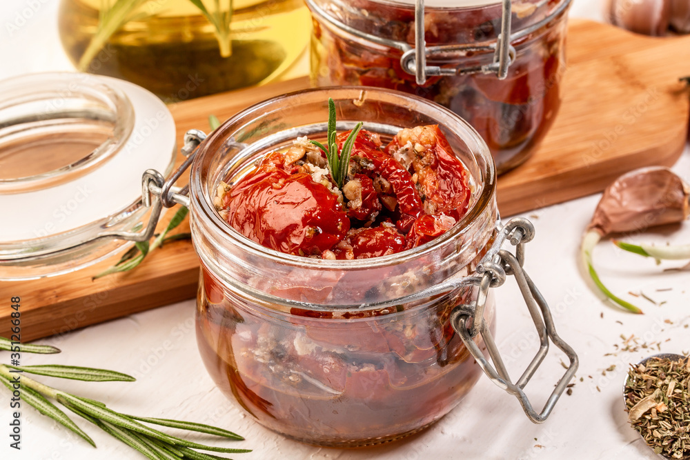 Food recipe background. Close up Sun dried tomatoes with garlic, oregano, olive oil in a jar on a light table, top view Food recipe background. Close up Sun dried tomatoes with garlic, oregano, olive oil in a jar on a light table, top view