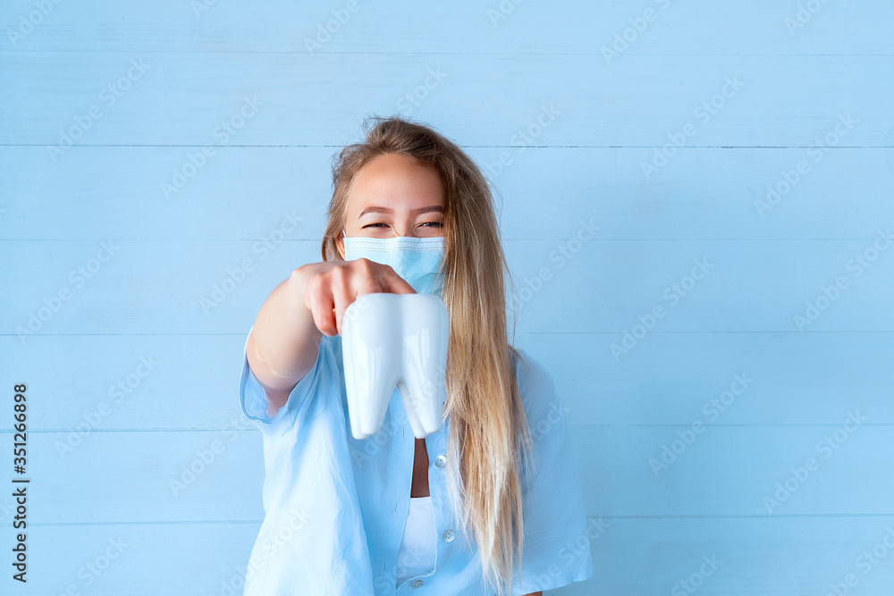 Human molar tooth Model. Female dentist in blue uniform holding tooth on blue background. Oral care concept, prevention of dental caries Human molar tooth Model. Female dentist in blue uniform holding tooth on blue background. Oral care concept, prevention of dental caries