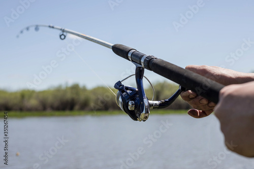 Fishing on the lake. Fishing rod with a reel in the hands of a fisherman on the background of the lake. A fishing background.