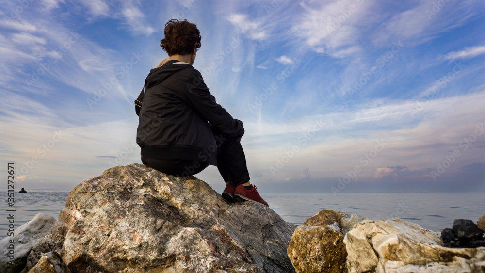 Obraz premium Old sad depressed woman sit alone on rocks, looking at distant sea / seascape horizon. Time to go, say goodbye. Miss someone. Desire, hope to go far away. Unhappy woman feel lonely at seaside outdoor
