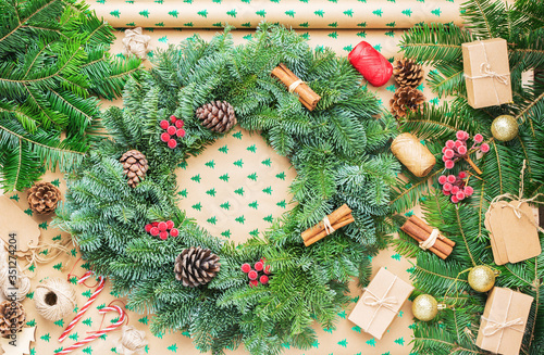 Top view of Christmas wreath on wrapping paper background, various accessories including fir tree branhes, pinecones and presents, selective focus photo