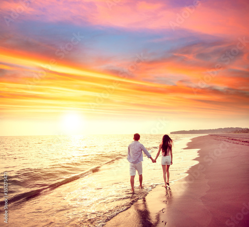 young couple walking on the beach at sunset
